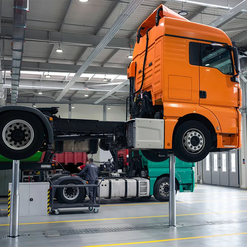 Orange articulated truck elevated on hydraulic lift inside Al Saha's heavy vehicle repair workshop in UAE